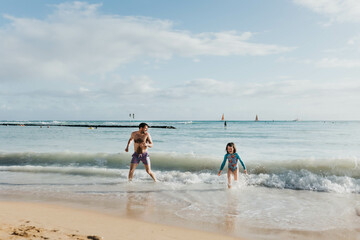 Father and daughter play in ocean on beach in Waikiki