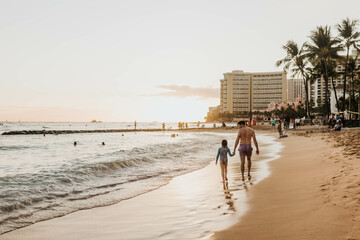 Father and daughter hold hands while they walk along beach at sunset