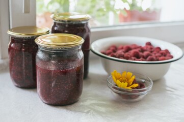 Glass jars of raspberry jam and bowl of red raspberries