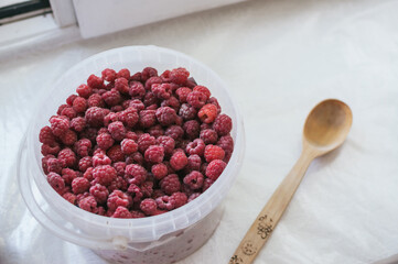 Ripe raspberries in bucket and wooden ladle on windowsill