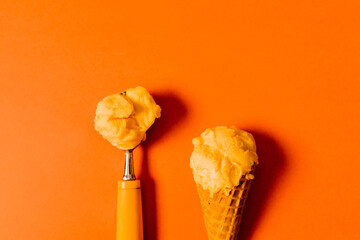 Orange sorbet in scoop and waffle cone with bright orange background