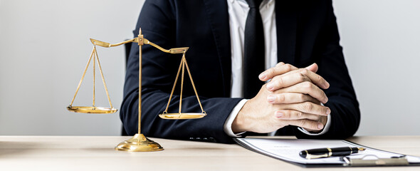 A male lawyer sits in the office of his law firm, on a table with a scale of justice and a hammer...