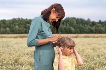 family photo. mom combs and braids her daughter's hair in the summer in the field. summer family walks