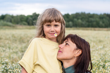 Fototapeta premium portrait of a mother and daughter in a summer field. a woman and a girl collect daisies in a chamomile field. children and parents