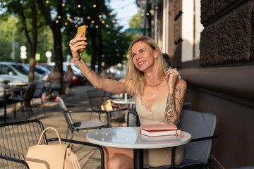 A blonde with a tattoo on her arm sits in a summer cafe and emotionally talks on the phone via video communication. Blogger concept