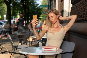 A blonde with a tattoo on her arm sits in a summer cafe and emotionally talks on the phone via video communication. Blogger concept