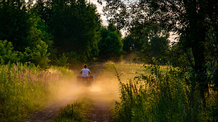 young man driving a quad bike down a dirt road at sunset © Remigiusz Góra