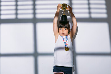 Dark-haired girl with sports championship medals, raising her trophy cup with her hands, over the...