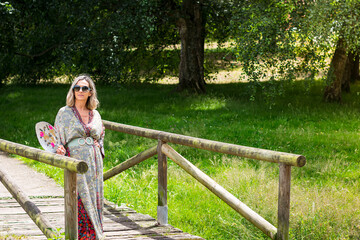 Naklejka premium Blonde woman posing in a long dress on a wooden bridge in a park in Asturias, Spain.The photograph is taken in horizontal format.
