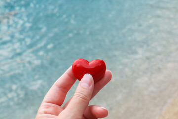 Red heart in woman hand with sea in background