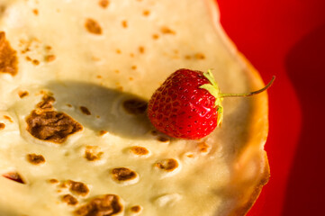 Ripe fresh strawberries on a thin pancake in a red plate, close-up.
