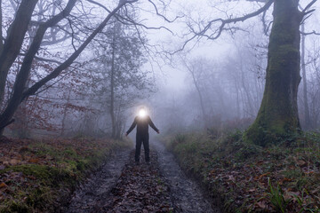 A spooky, hooded figure with a bright light coming from their head. In a forest on a foggy winters...
