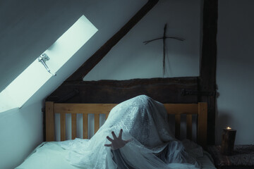 A spooky, ghostly figure sitting on a bed, with a hand reaching out with a cross above the bed.
