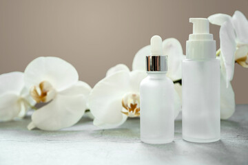 White glass serum bottle and lotion pump bottle with dispenser mock-up in the bathroom with orchid flowers in the background, unbranded cosmetic products, spa cosmetic product branding mockup