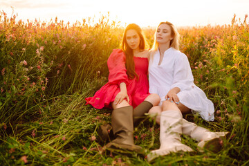 Portrait of two fair-haired girls in fashionable and stylish dresses in the blooming field. Nature, vacation, relax and lifestyle. Fashion concept.