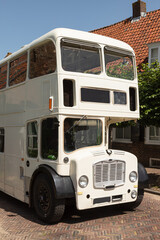 White high double decker bus rides over the narrow dike through the picturesque village of Amerongen