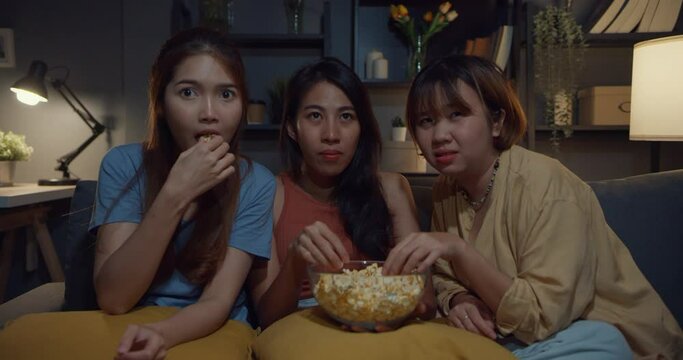 Group of attractive Asia lady girl freaking out fear and terrified moment eat popcorn watch horror online movie on couch in living room at home in night. Weekend lifestyle activity quarantine concept.