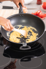 Close up female afro american hands stirring eggs on a deep frying pan