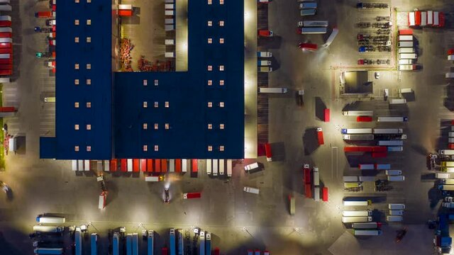 Aerial top down view hyper lapse (hyperlapse - motion time lapse) of a logistics park with a loading hub. Semi-trailer trucks stand at warehouse ramps for load and unload goods at night