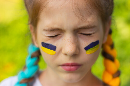 the face of a girl with closed eyes and with yellow-blue national flags of Ukraine painted on her cheeks. concept of Ukrainian patriotism, independence day. sports and fan support.