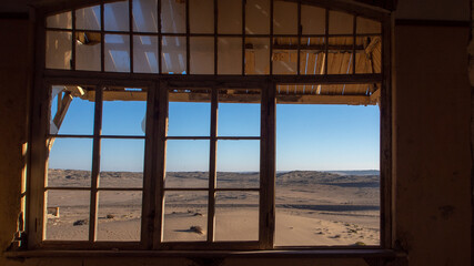 Desert view through on of the neglected window frames of a house at the ghost town of Kolmanskop, Namibia