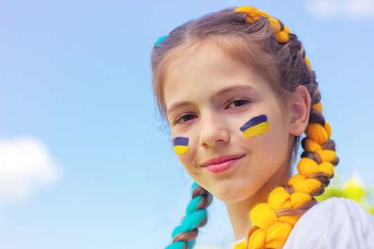 smiling Ukrainian girl with blue and yellow flags painted on her face against the sky with copy space. patriotism concept, flag day and independence day of Ukraine. sports and support of fans.
