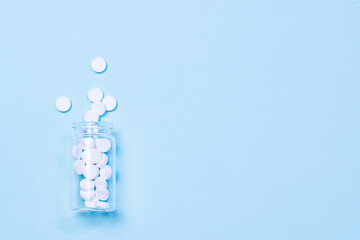 White round medical tablets in transparent glass bottle on light blue background with copy space for your design. Treatment and health care concept.