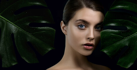 Young woman with perfect skin arounded by tropical green leaves on dark background. Beautiful...