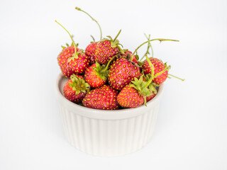 Appetizing fresh strawberries with green cuttings and twigs lie in a white bowl on a white background. Isolate. Cutout. Natural red berry. Vegetarian snack. Horizontal