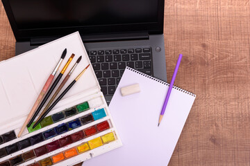 Online drawing class cover concept with laptop, sheet of paper, paints and brushes on wooden office desk. Online education