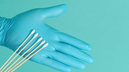 One Cotton stick for swab test in hand with blue medical gloves or latex glove on mint green or Tiffany Blue background.covid-19 concept. close up