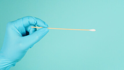 One Cotton stick for swab test in hand with blue medical gloves or latex glove on mint green or Tiffany Blue background.covid-19 concept. close up