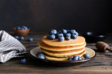 Homemade pancakes on a wooden background with honey and blueberries.