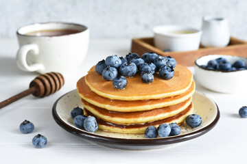 Homemade pancakes on a white plate with honey and blueberries for breakfast. Good morning!