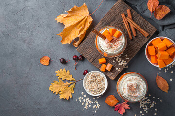 Two servings of pumpkin parfait with cream and cocoa on a dark gray background with autumn leaves. Top view, copy space.