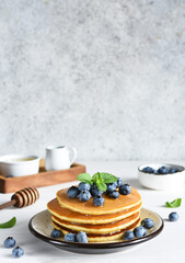 Homemade pancakes on a white plate with honey and blueberries for breakfast. Good morning!
