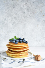 Homemade pancakes on a white plate with honey and blueberries for breakfast. Good morning!