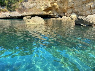 Paradise blue lagoon with cave grotto in Mediterranean sea. Turquoise sea and rocks idyllic summer landscape. Azure crystal clear sea water. Glittering sea rippled waves. 
