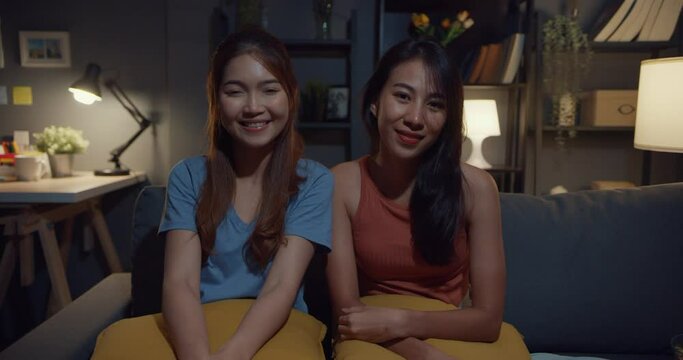 Teenager Asia women feeling happy smiling and looking to camera while relax in living room at home night. Cheerful Roommate ladies video call with friend and family, Lifestyle woman at home concept.