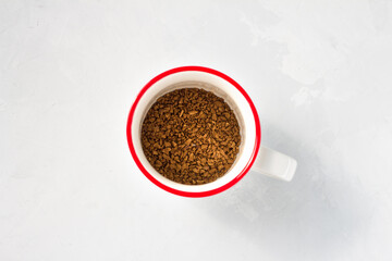 Dry instant coffee in a white cup with a red border on a gray plastered background, close up, top view
