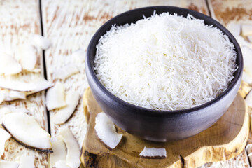 grated coconut inside a clay bowl, with coconut and coconut pieces in the background, culinary ingredient for sweets