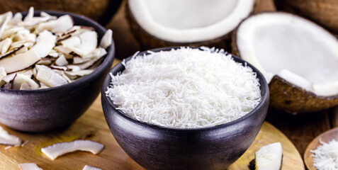grated coconut inside a clay bowl, with coconut and coconut pieces in the background, culinary ingredient for sweets