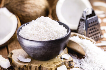 grated coconut inside a clay bowl, with coconut and coconut pieces in the background, culinary ingredient for sweets
