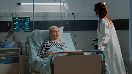 African american medic fixing adjustable bed for patient in hospital ward at medical clinic. Unwell old man with nasal oxygen tube looking at modern tablet for examination results