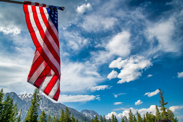 American flag in Yellowstone National Park surrounded by trees and mountains.