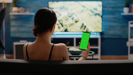 Caucasian woman holding mobile phone with green screen vertically looking at mockup template for chroma key. Young person using modern smartphone with copy space of isolated background