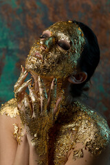 Girl with a mask on her face made of gold leaf. Gloomy studio portrait of a brunette on an abstract background.