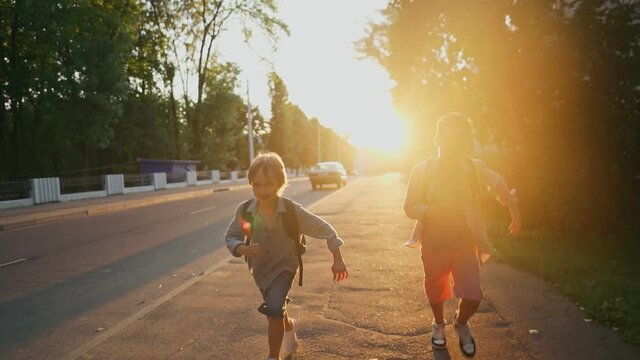 Two schoolboys with a backpacks running on street at sunset time. Back to school. High quality 4k footage