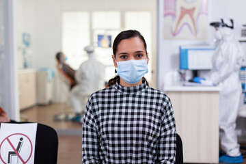 Fototapeta na wymiar Portrait of woman in dental office looking on camera wearing face mask sitting on chair in waiting room clinic while doctor working. Concept of new normal dentist visit in coronavirus outbreak.