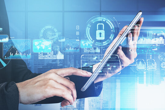 Businessman hand holds tablet device, blue hologram glowing digital information security interface. Concept of cyber security and data storage. Padlock and business symbols. Panoramic office